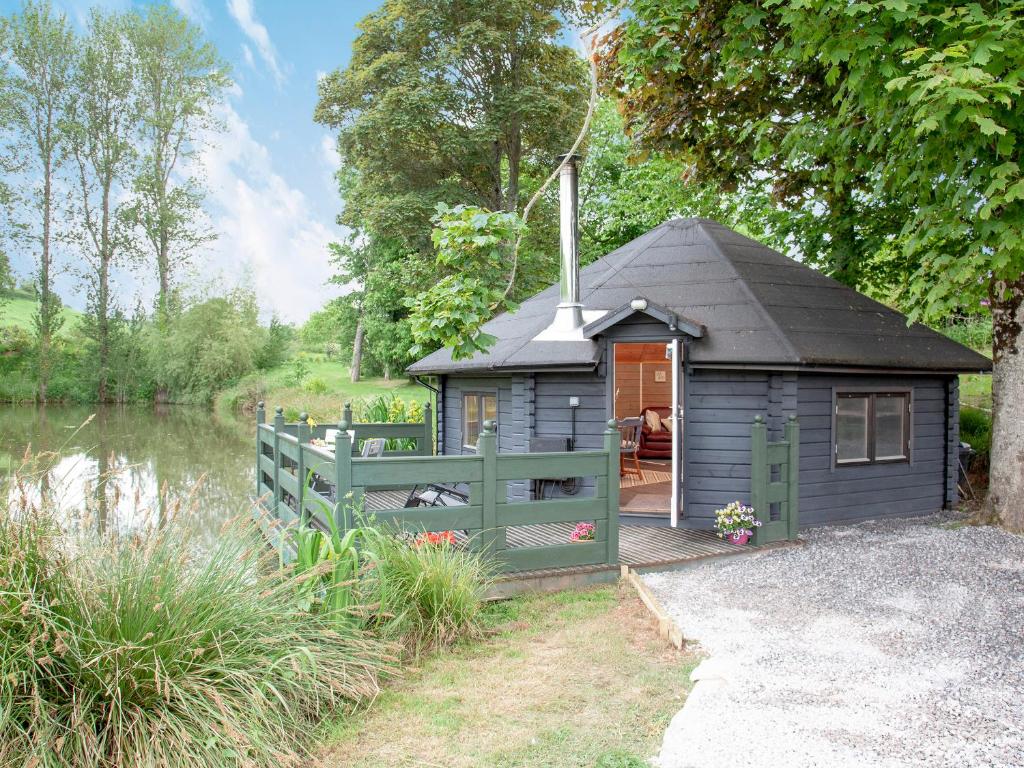 a blue building with a black roof next to a river at Mallard Roundhouse - Uk33891 in Cullompton