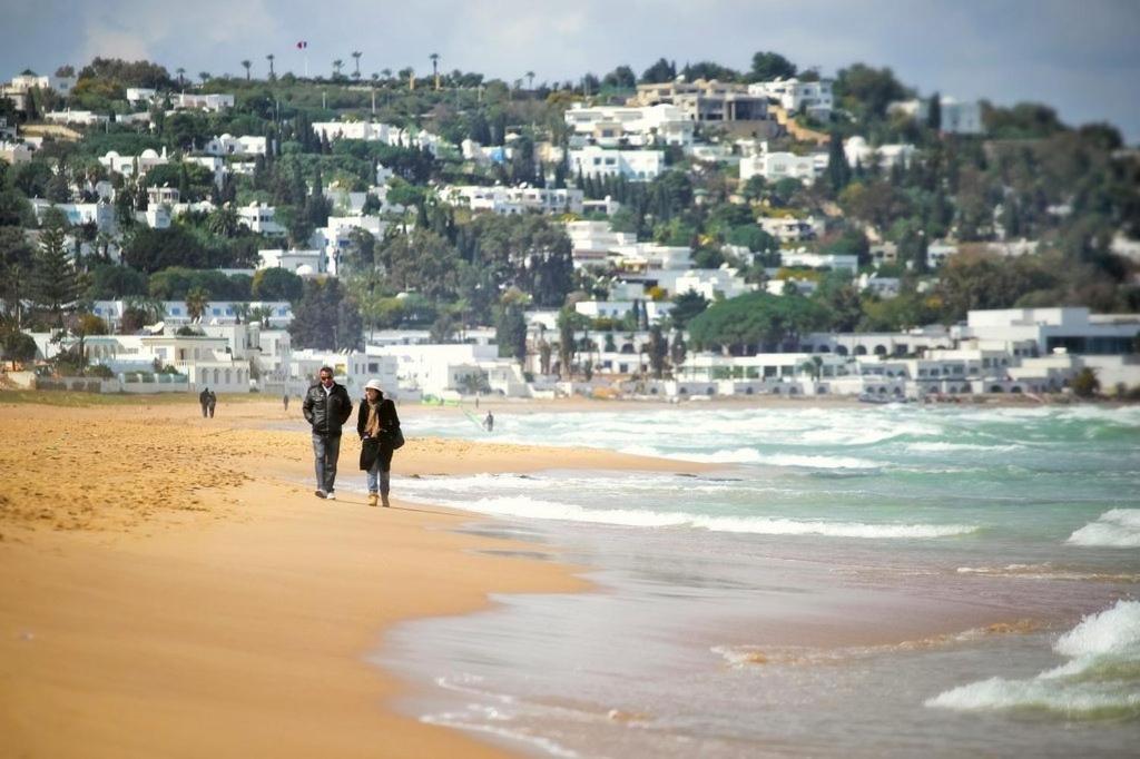 two people walking on a beach with buildings in the background at Villa Victoria in Tunis