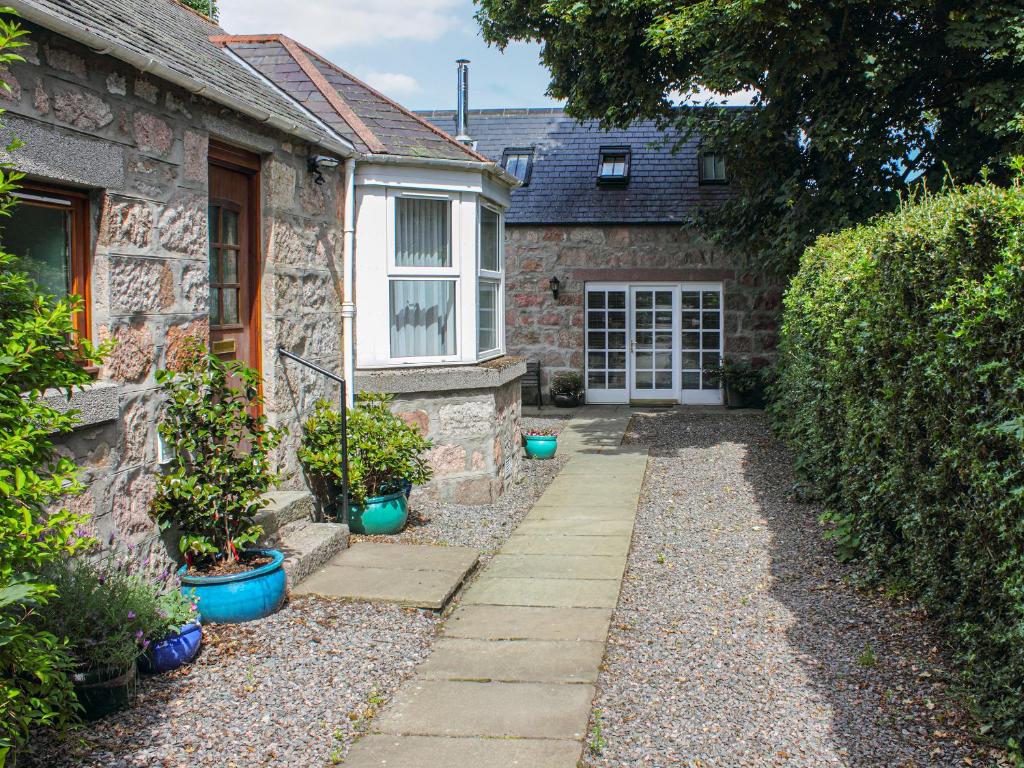 una casa de piedra con una puerta y algunas plantas en Pine Tree Cottage - Uk45925, en Ballater