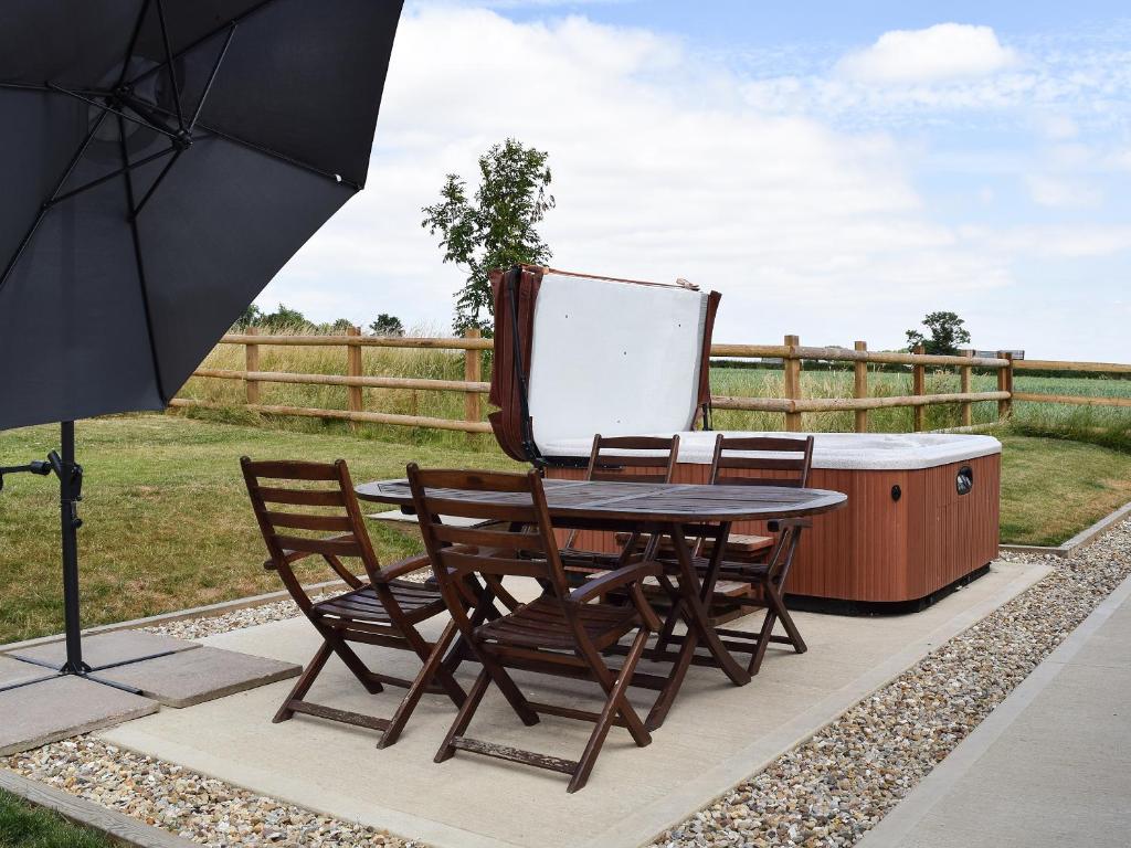 un patio con tavolo, sedie e ombrellone di Waxwing Cottage a Foxton
