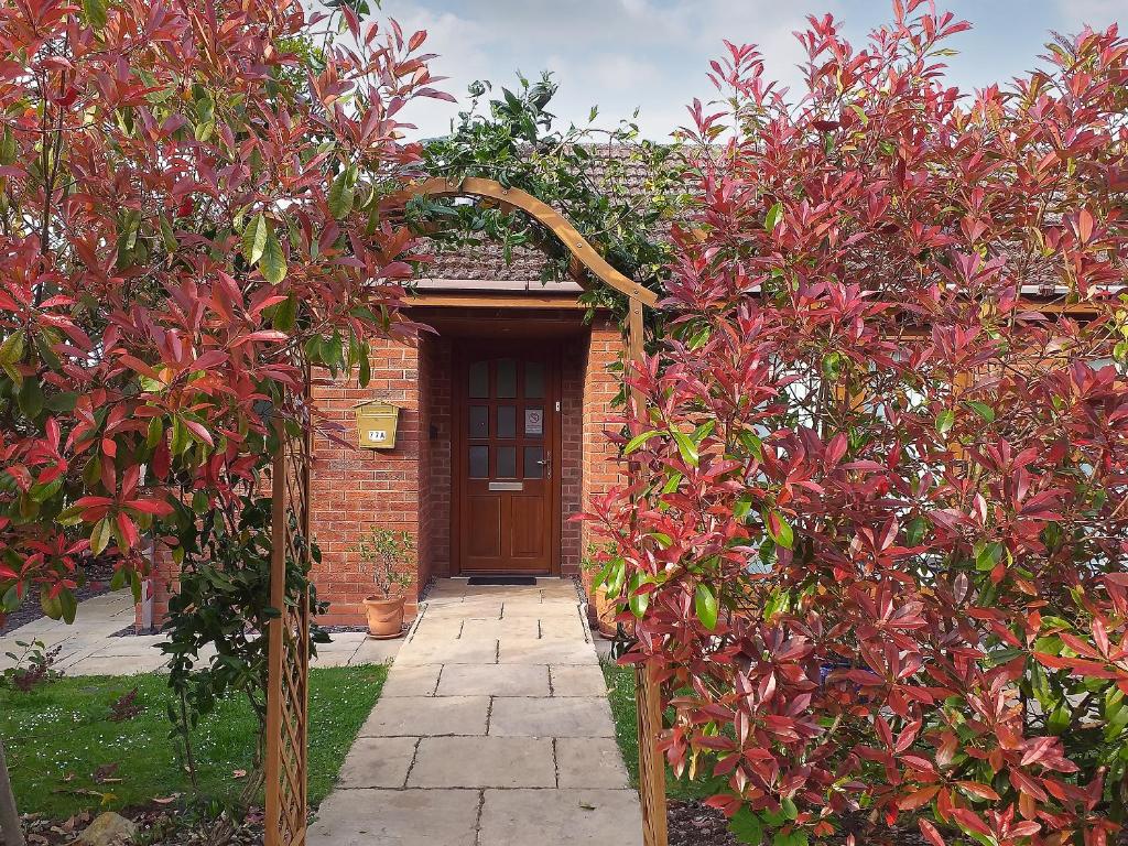 an archway in front of a house with red bushes at Little Acorns in Great Malvern