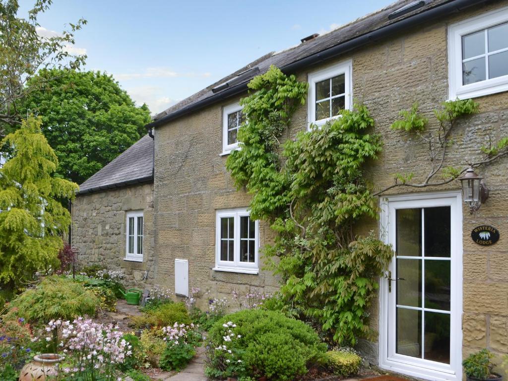une maison en briques avec des fenêtres blanches et des plantes dans l'établissement Wisteria Cottage, à Alnham