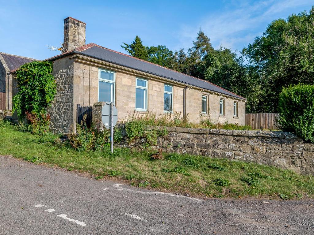 a brick house with a stone wall and a street sign at Shawdon Hill Cottage in Glanton