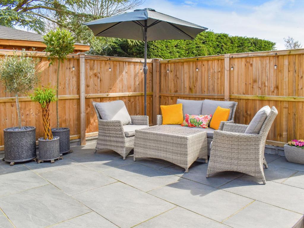 un patio con sillas de mimbre y sombrilla en The Den, en Herne Bay