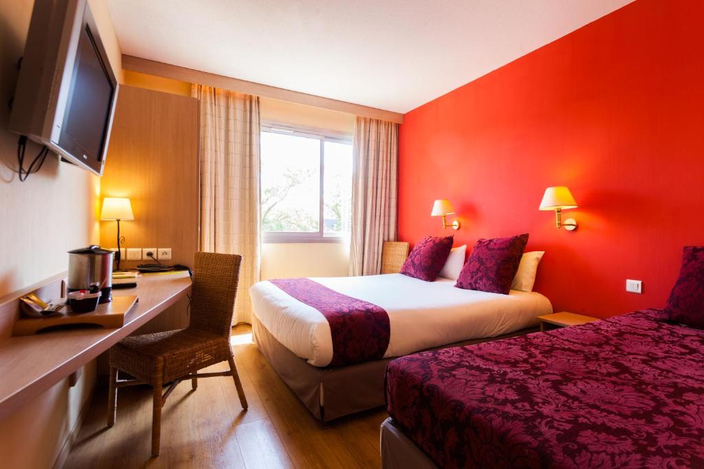 um quarto de hotel com duas camas e uma escrivaninha em Logis NIMOTEL Hôtel Cosy em Nîmes