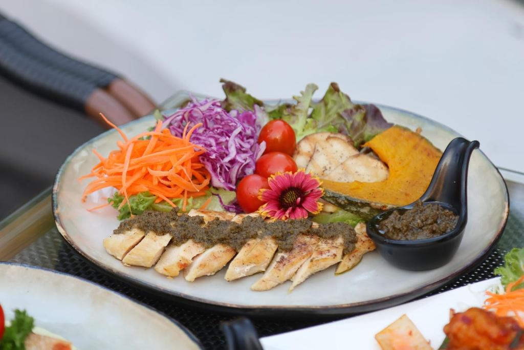 A plated fish and vegetable meal with salad and dipping sauce.