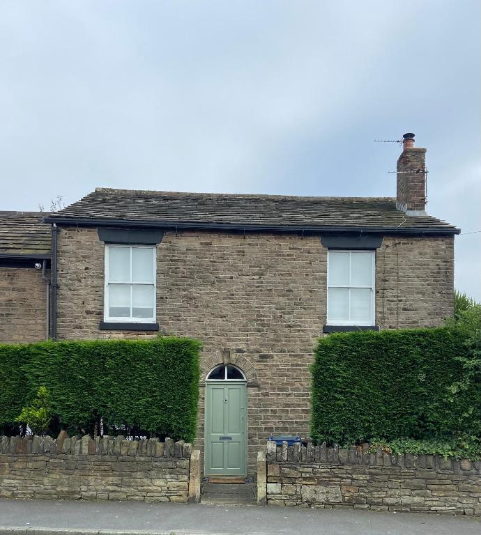 a brick house with a green door and bushes at Old Store Cottage, Up Holland in Upholland