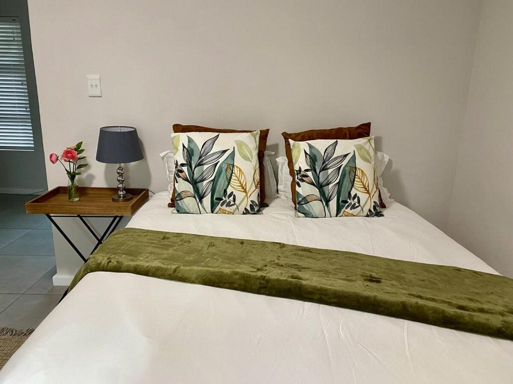 a bed with two pillows and a table with a lamp at Garden flat Durbanville - with Office, WiFi and secure gated parking in Eversdal