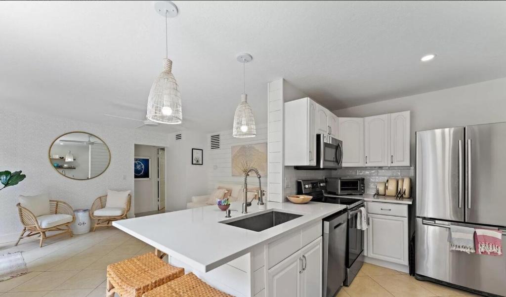 a kitchen with white cabinets and a stainless steel refrigerator at Beachside Modern Wellness Villa with Spacious Patio in Jupiter