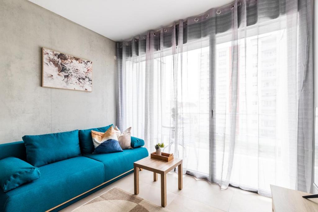 a blue couch in a living room with a large window at A26 Condo by the Rhine and 3-countries-bridge in Huningue