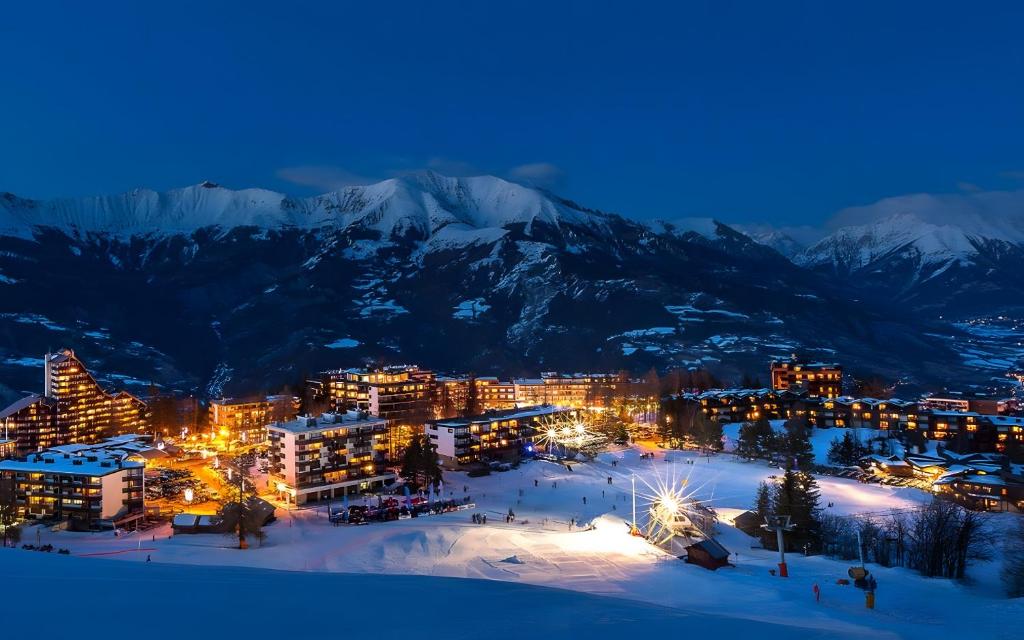 eine Stadt im Schnee bei Nacht mit schneebedeckten Bergen in der Unterkunft Studio au coeur de Praloup 1500 in Uvernet
