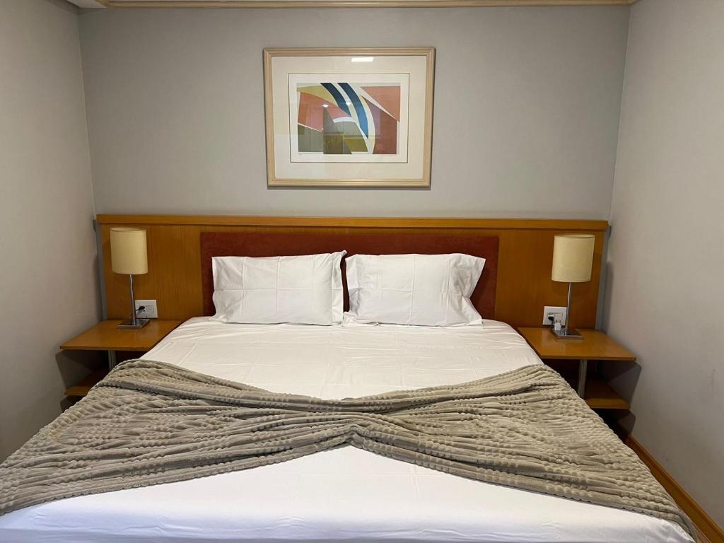 a bedroom with a bed with two nightstands and two lamps at Hotel Bienal Flat Executivo - UH 304 in Sao Paulo