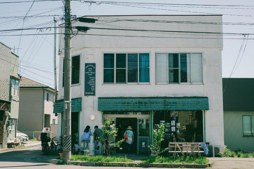 Un bâtiment blanc avec des personnes debout à l'extérieur dans l'établissement CORNER SHOP Miyota, à Miyota