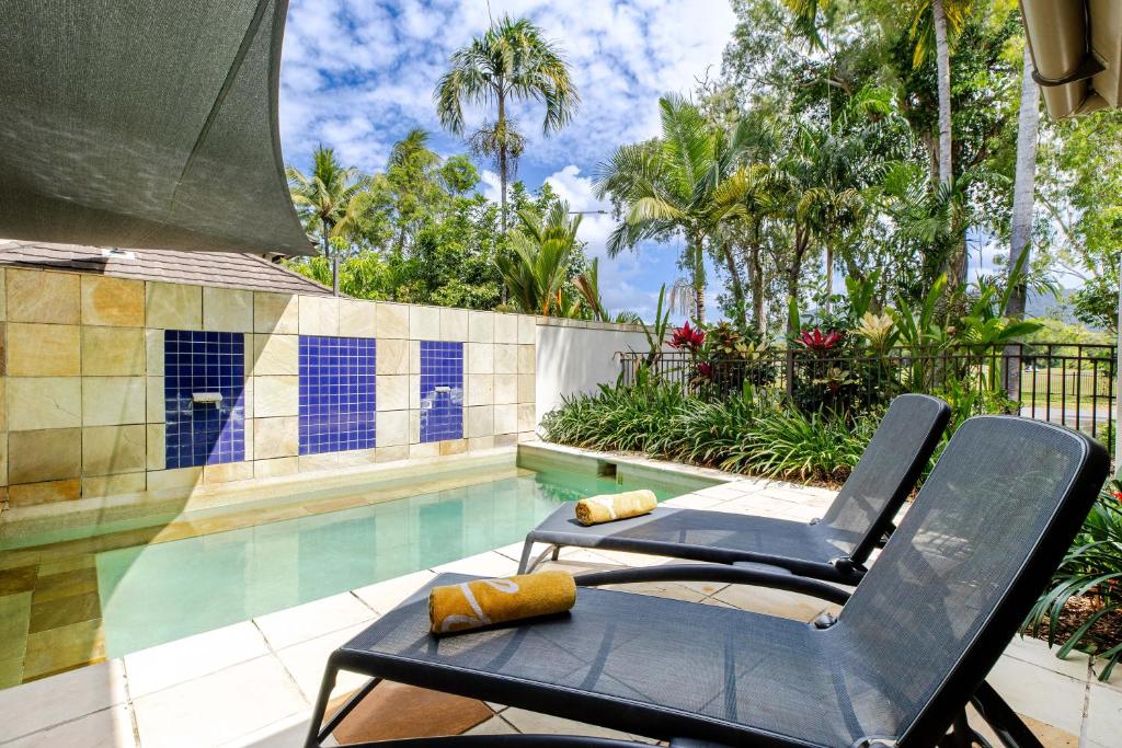 a pool with two chairs next to a swimming pool at Tranquil Waters 2 Bedroom Apartment in Port Douglas