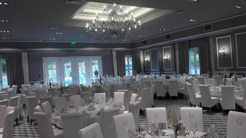 a banquet hall with white tables and chairs and a chandelier at Grand Meteora Hotel in Kalabaka
