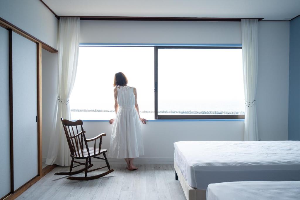 大山町にあるDAISEN UMIHOTARU Entire houseの寝室に立って窓の外を眺めている白いドレスを着た女性