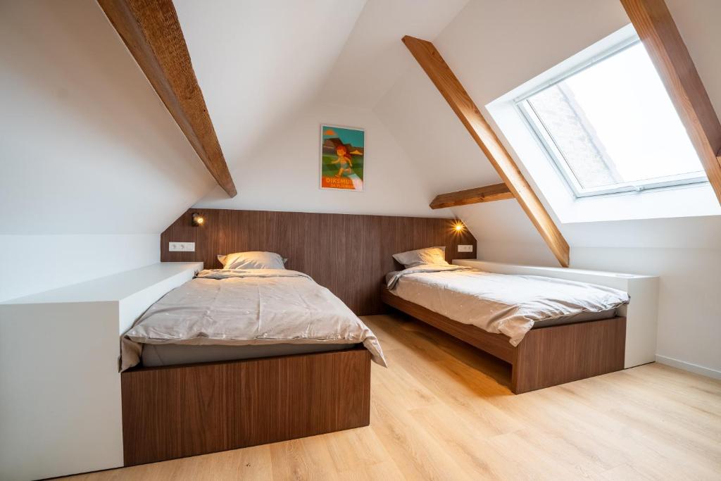 two beds in a attic bedroom with a window at Mademoiselle Julie in Diksmuide