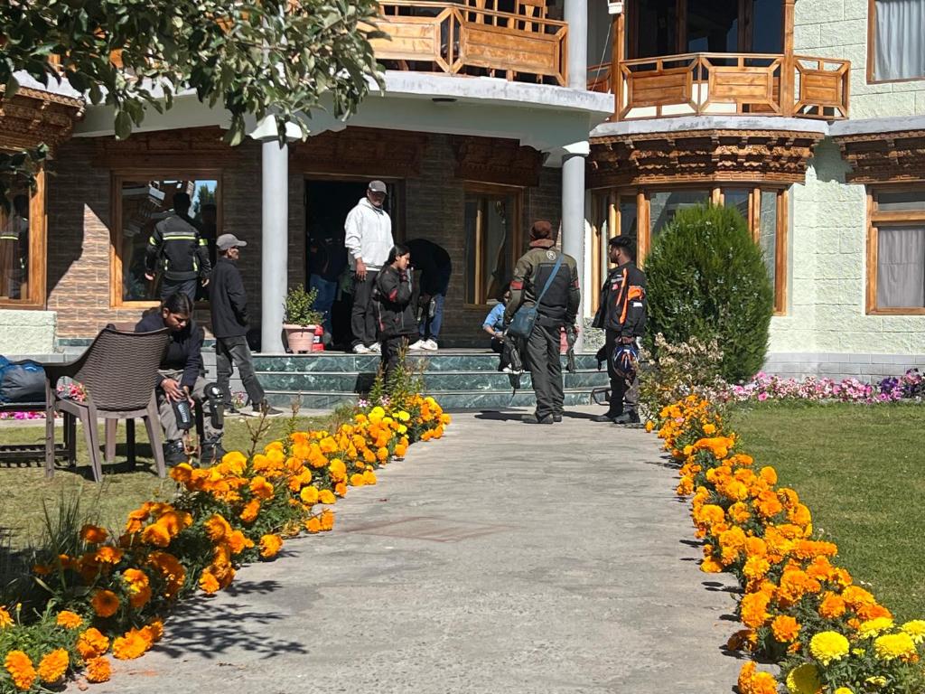 a group of people standing outside of a building with flowers at Mandalchan hotel in Leh