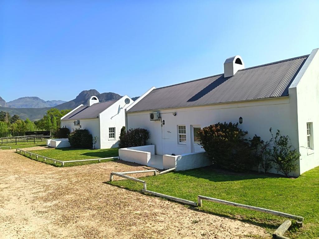 a white farm house with a gravel driveway at La Jolie Dauphine Guest House in Franschhoek