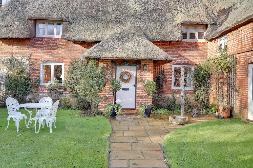 a thatched house with a table and chairs in the yard at Lake Cottage in Swindon