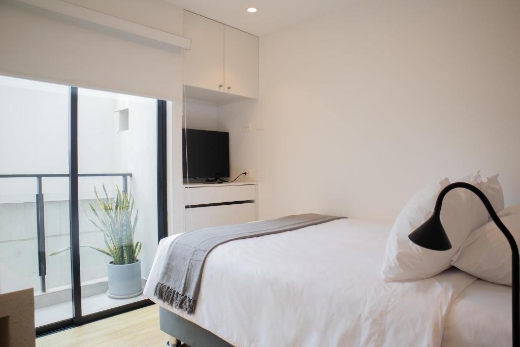 a white bedroom with a bed and a television at Seaside Studio 1BR near the Malecon in Miraflores in Lima