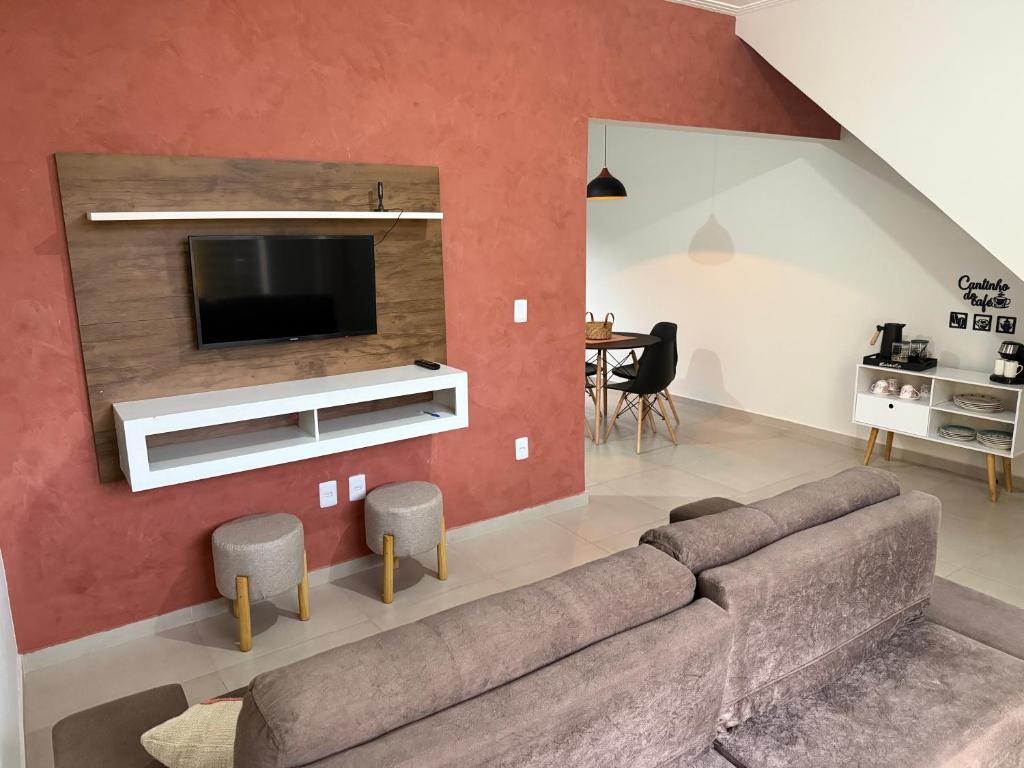 Una sala de estar con un sofá y un televisor en una pared. en Conforto a 8min da Canção Nova com Garagem, en Cachoeira Paulista