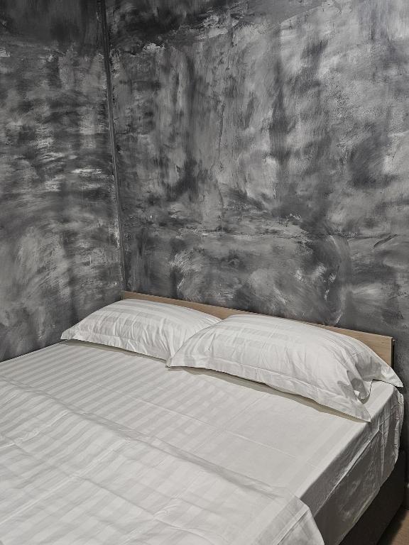 a bed with white sheets and a gray wall at The Cozy Hotel in Sungai Petani