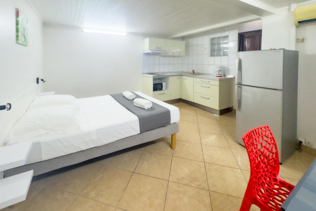 a bedroom with a bed and a refrigerator and a red chair at Studio 2 - Bougainvillée - proche plage in Lazaret