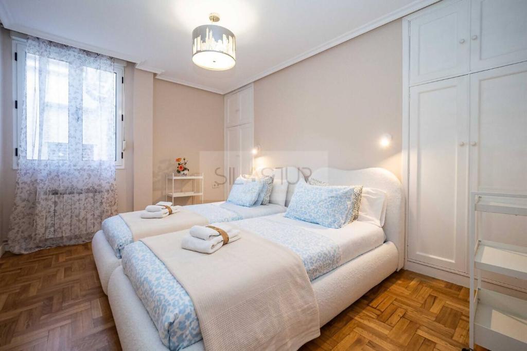 a white bedroom with two beds and a window at Nuevo Luanco By Silastur in Gijón