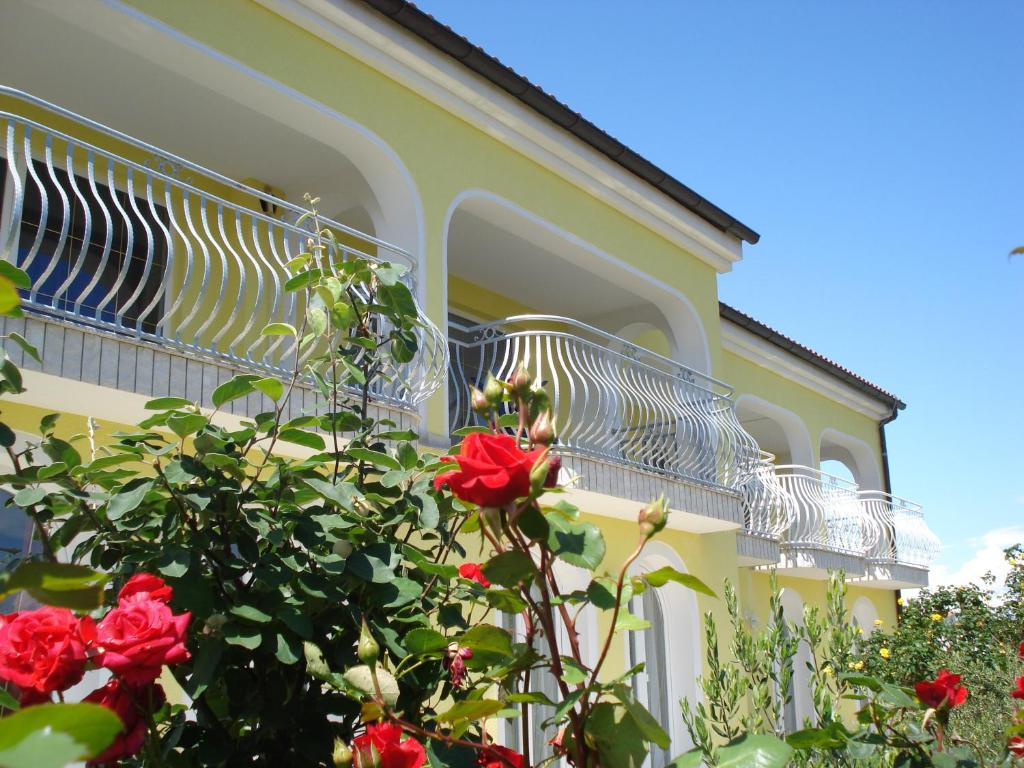 a yellow building with a balcony with red roses at Ana Rooms in Krk