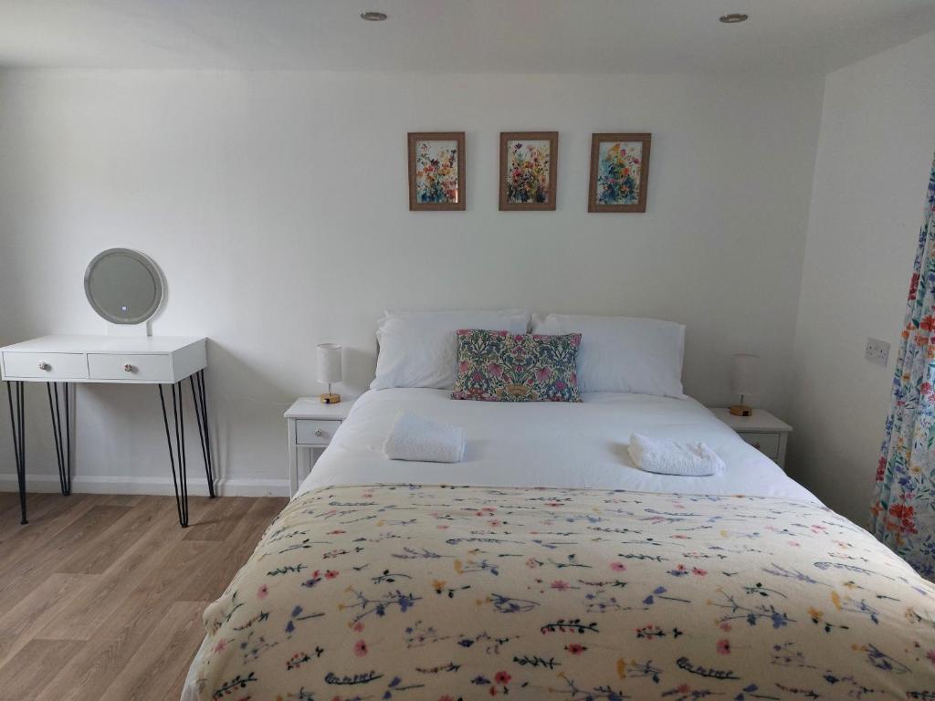 1 Schlafzimmer mit einem weißen Bett, 2 Tischen und einem Spiegel in der Unterkunft The Garden Room at Poplar Cottage in Wick Saint Lawrence