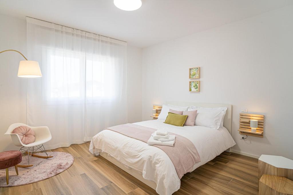 a white bedroom with a large bed and a chair at Residenza JOY in Pordenone