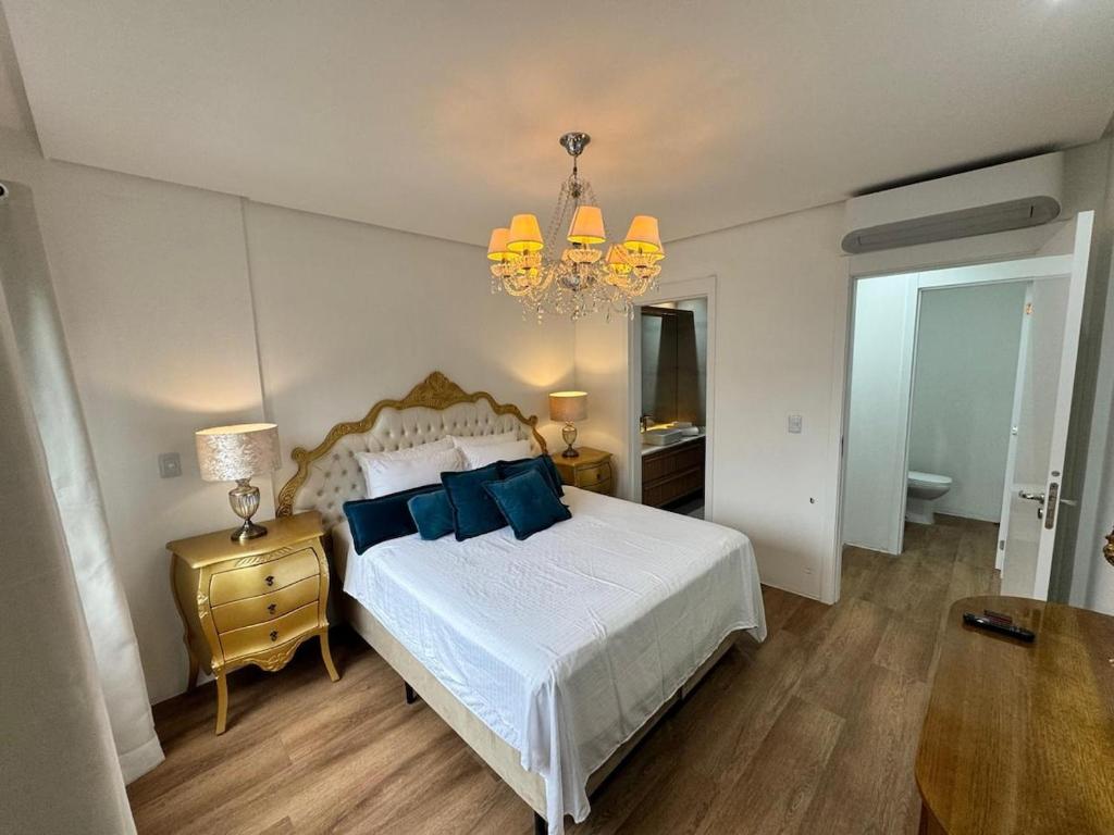 a bedroom with a bed with blue pillows and a chandelier at Apartamento 800m da Rua Coberta in Gramado