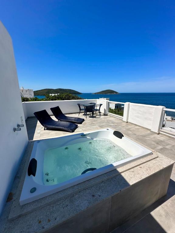 a hot tub on a patio with the ocean in the background at Greek House Premium in Arraial do Cabo