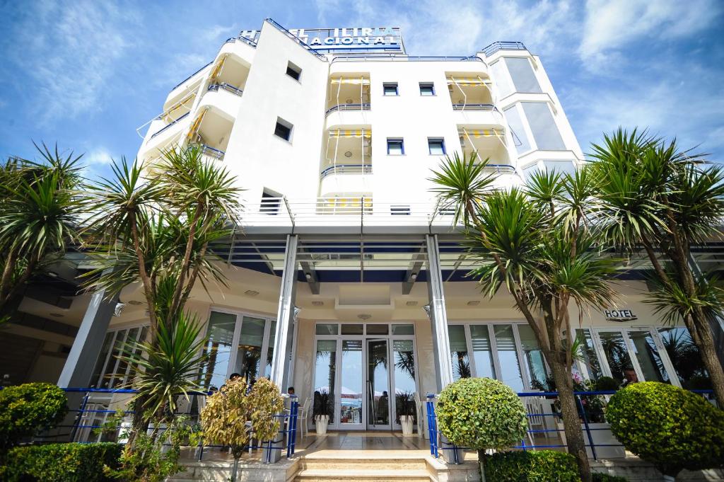 ein weißes Gebäude mit Palmen davor in der Unterkunft Iliria Internacional Hotel in Durrës