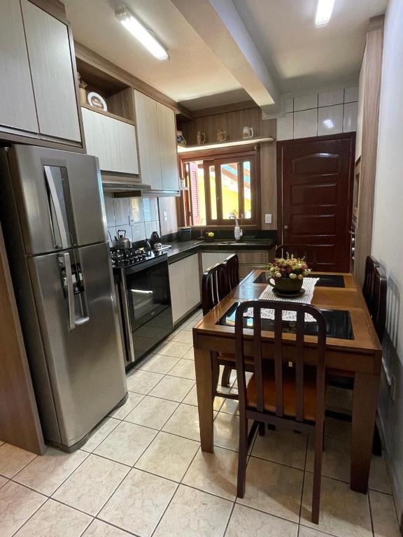 a kitchen with a table and a stainless steel refrigerator at Casa de veraneio 2 dormitórios in Torres