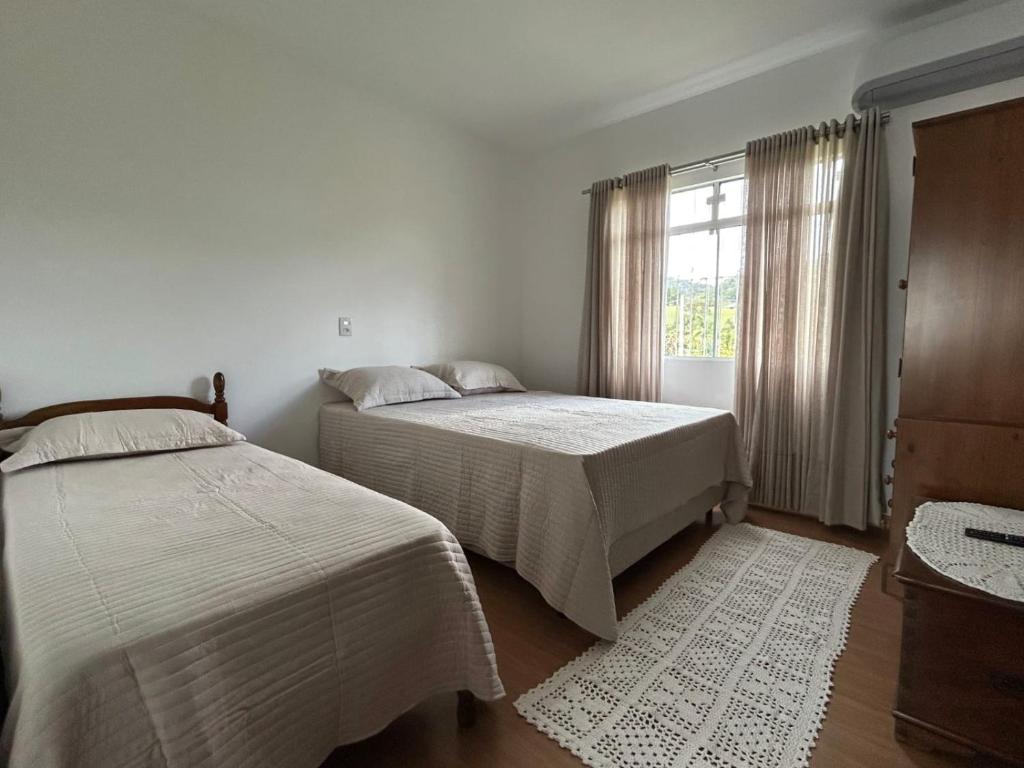 two beds in a white room with a window at Morada dos Pomares in Pomerode