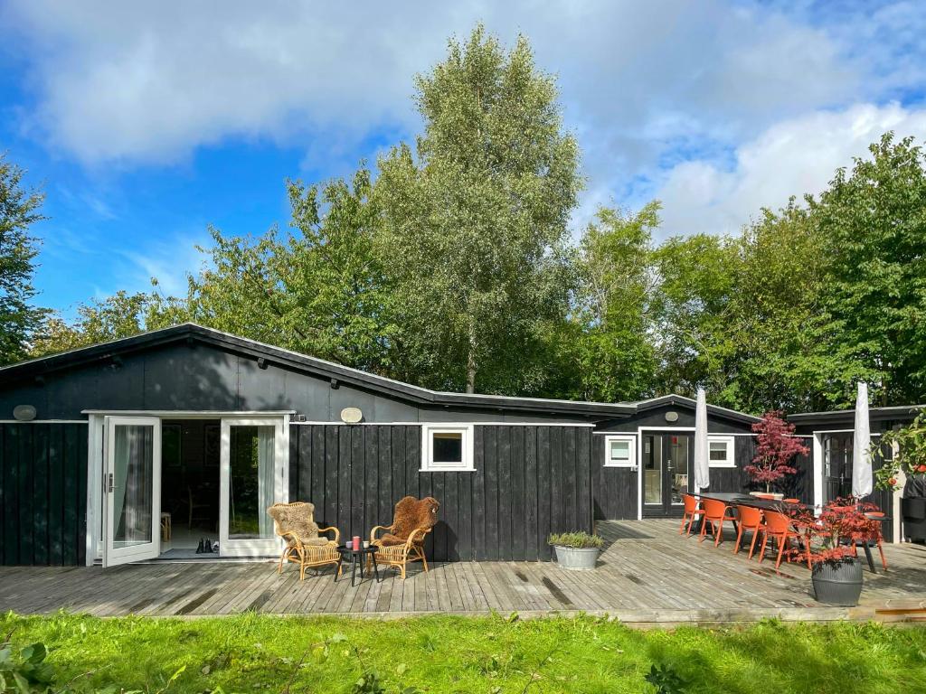 a black house with a wooden deck and chairs at Holiday Home Near Tisvilde Forest And Rhubarb Farm in Vejby Strand
