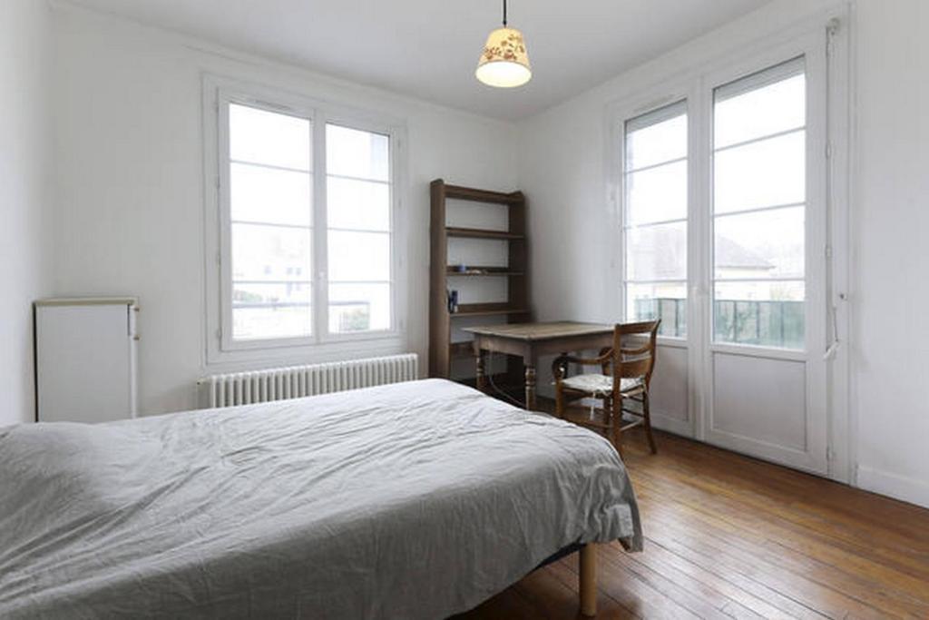 a bedroom with a bed and a desk and windows at Chambres meublées chez l'habitant dans appartement proche gare sncf in Creil