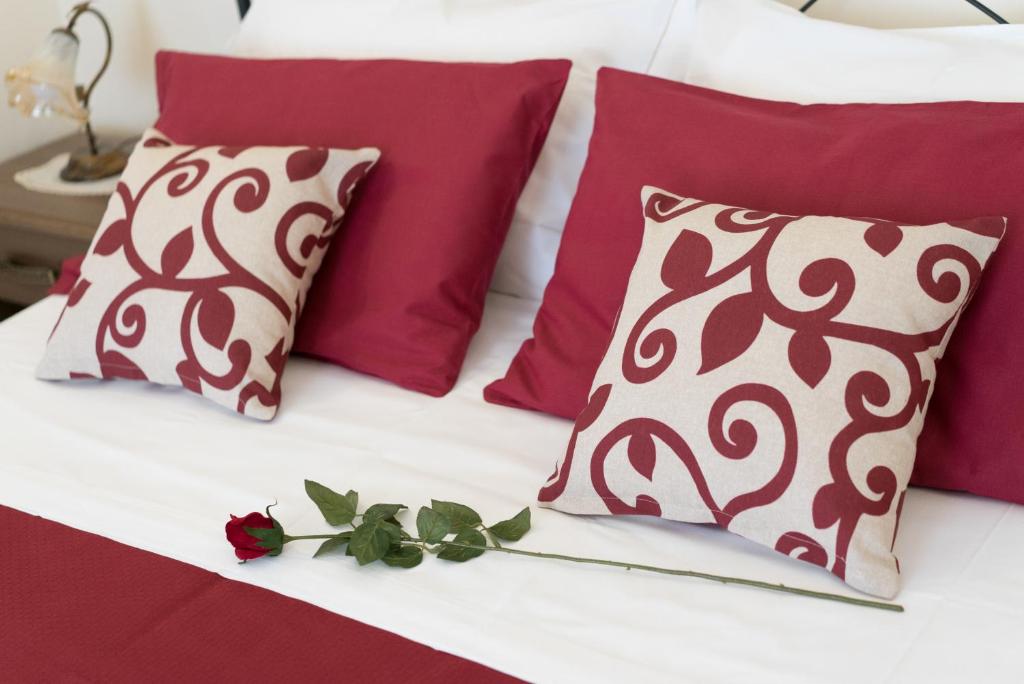 Una cama con almohadas rojas y blancas y una rosa. en B&B Palazzo Tornabene, en Catania