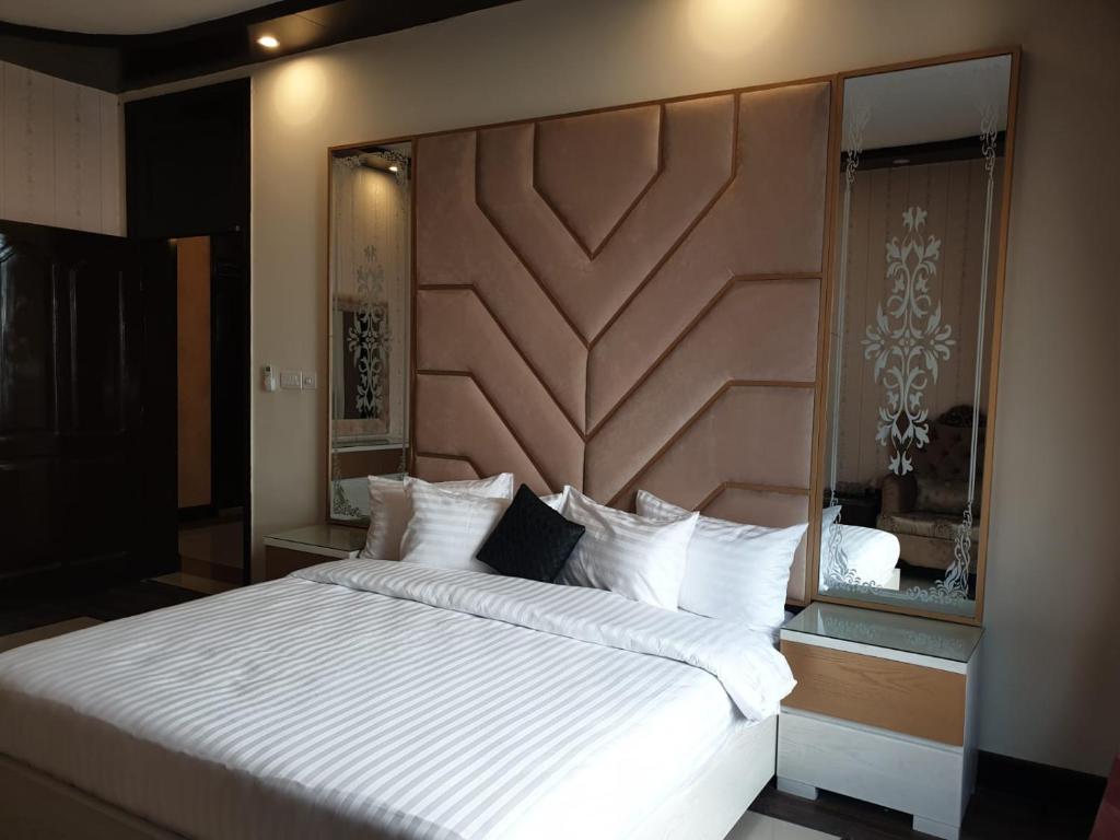 une chambre avec un grand lit blanc avec une tête de lit en bois dans l'établissement Royal Villa Islamabad, à Islamabad