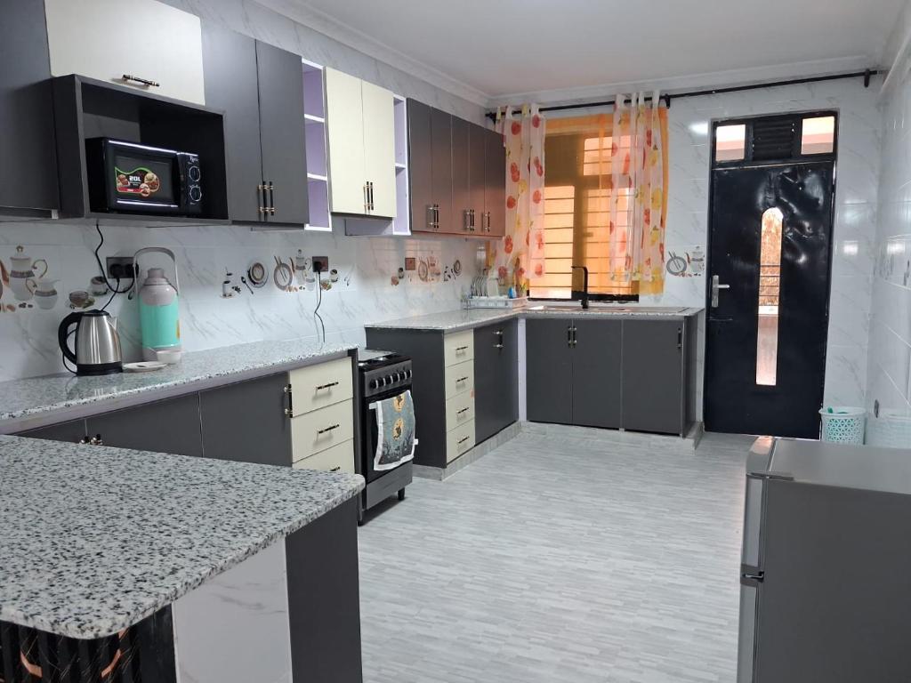 une grande cuisine avec des comptoirs blancs et des placards gris dans l'établissement Moonshine walkers furnished apartments, à Naivasha