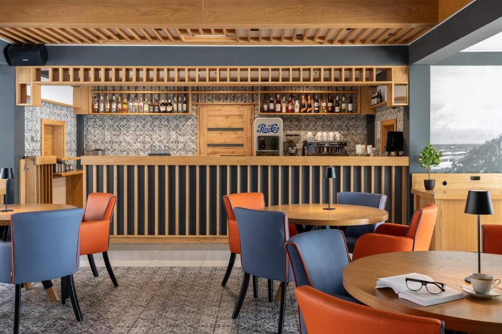 Contemporary bar lounge with wooden counter, bottle display, round tables, blue and orange armchairs.