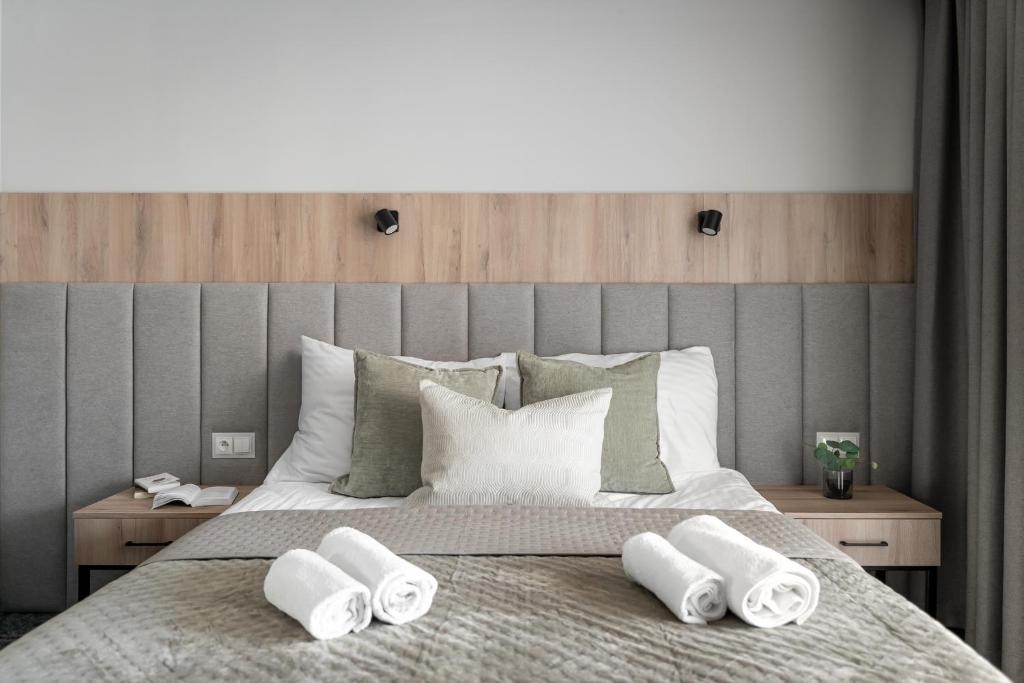 Symmetrical bed view with gray padded headboard, decorative pillows, and three rolled towels.