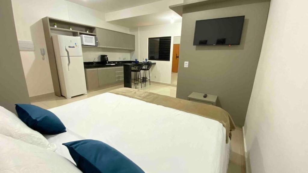 a bedroom with a white bed with blue pillows and a kitchen at 308-1 · Suíte Luxo Unievangélica/Ânima. 308 in Anápolis
