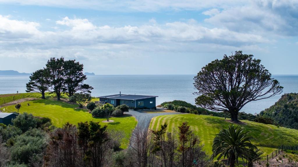 a blue house on a green hill with the ocean at The Kina Cottage in Tutukaka