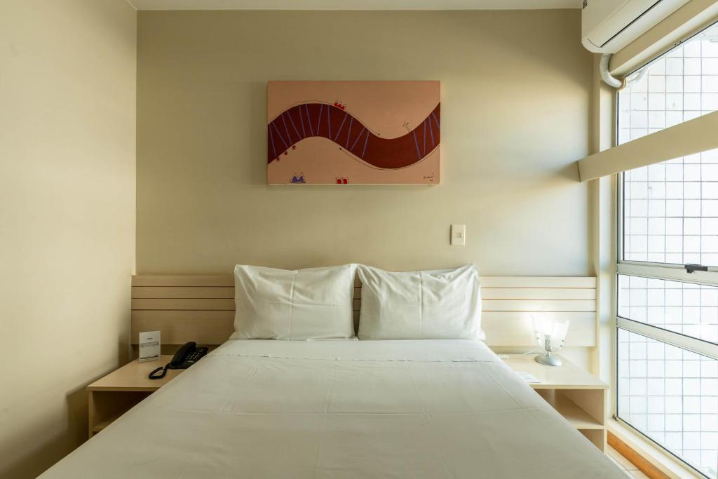 a bedroom with a bed with white sheets and a painting at Verona Hplus Long Stay in Brasilia