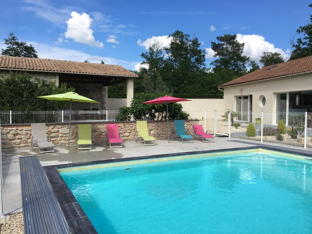 a swimming pool with chairs and umbrellas next to a house at Loft piscine chauffée et couverte in Sauvignac