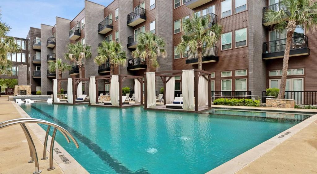 a swimming pool in front of a building with palm trees at Lookout Luxe 2BR | Shuffleboard | Classy | 1GB in Dallas