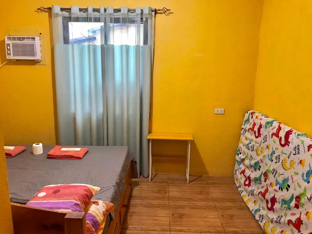 Una habitación amarilla con una cama y una ventana con cortina. en Three Sister's Inn, en Siquijor